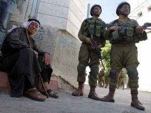 An elderly Palestinian man sits near Israeli soldiers taing part in a search operation for three Israeli teenagers believed kidnapped by Palestinian militants. Israel is using the search to root out remaining Hamas infrastructure in the West Bank.